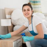 Happy Female Housekeeper Cleaning Nightstand In Room